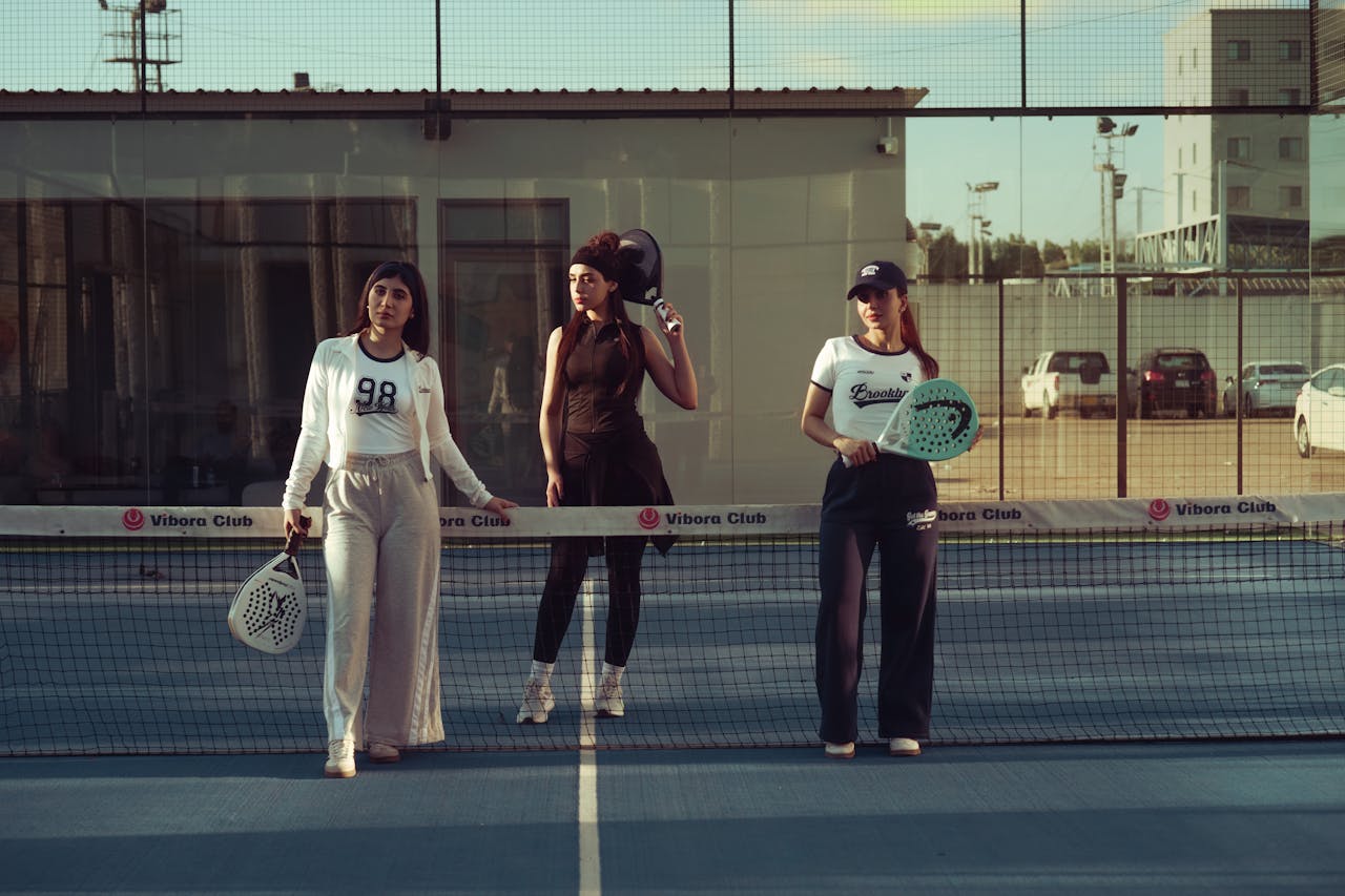 Three women with paddles standing on a tennis court during day.