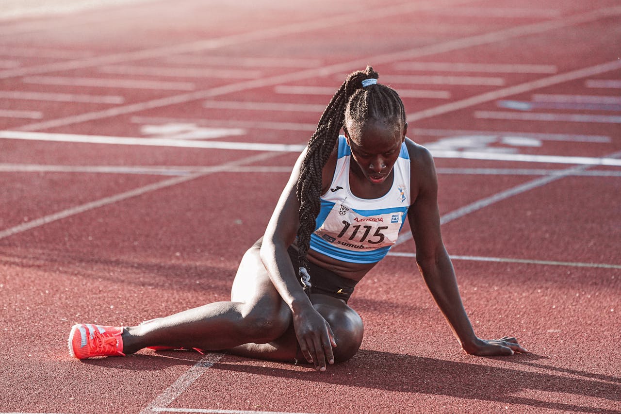 A female athlete in sports gear taking a break on the running track after a race, during daylight.