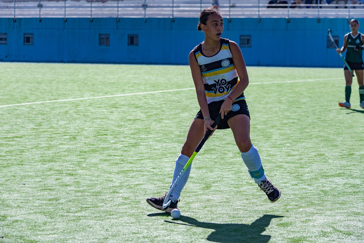 Young female field hockey player in action on an outdoor green field during a sunny day match.
